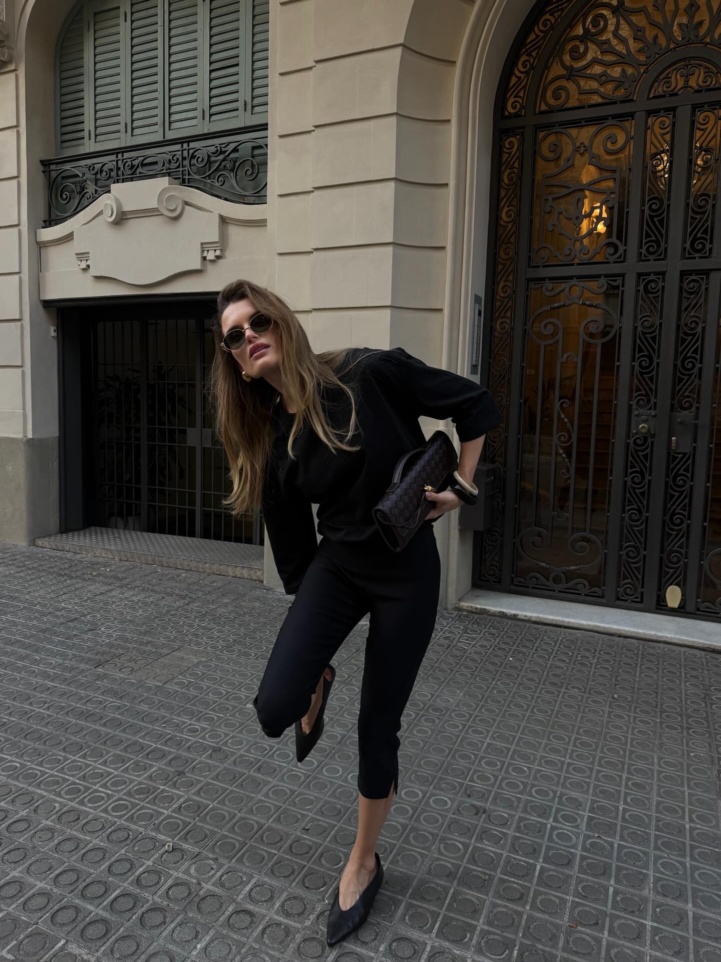 Woman wears black capri pants, high vamp heels, black sweater, clutch and sunglasses.