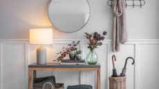 grey and white hallway with side table, circular mirror and coat hangers