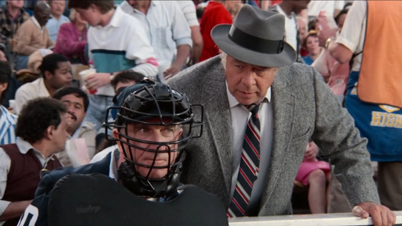 Leslie Nielsen in umpire gear with a man in suit standing behind him.