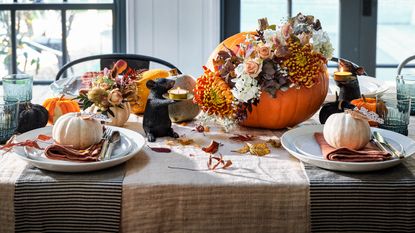  A pair of wellington boots, basket of pumpkins and dried autumn leaves on a doorstep outside a wooden clad building.