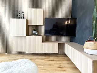 A living room with a wood panelled wall with cabinets fixed to it in a asymmetrical pattern