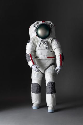 a white spacesuit with gray and red highlights stands against a gray background