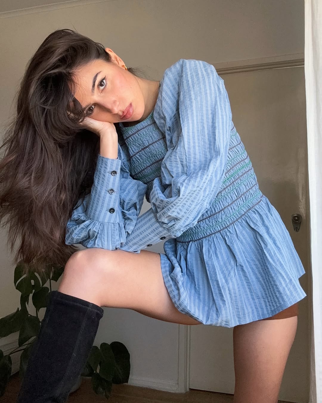 Tamara Mory shows off her voluminous hair while wearing a blue prairie-style top, brown shorts, and black boots