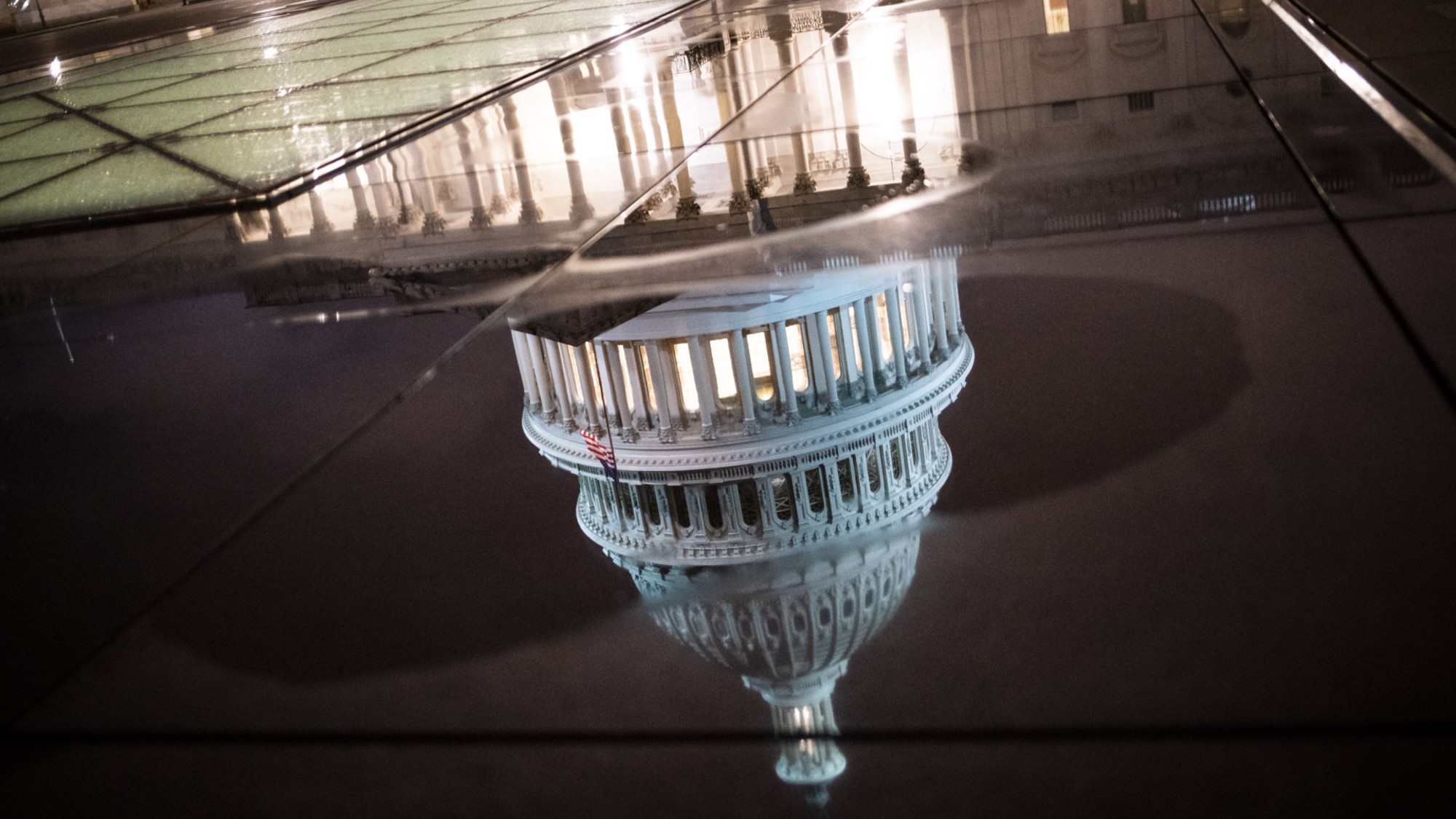 The U.S. Capitol building is reflected in a puddle at night in Washington, D.C.