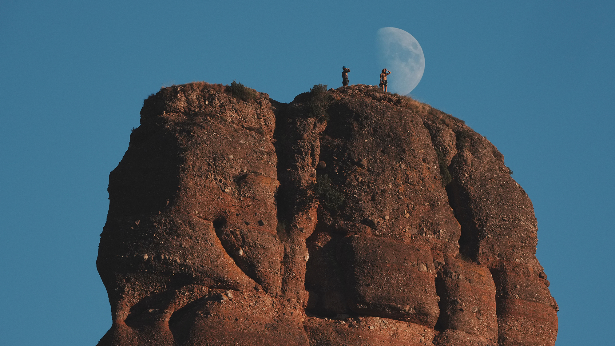 A pair of climbers stand atop the Cavall Bernat monolith in the Montserrat massif of northeast Spain