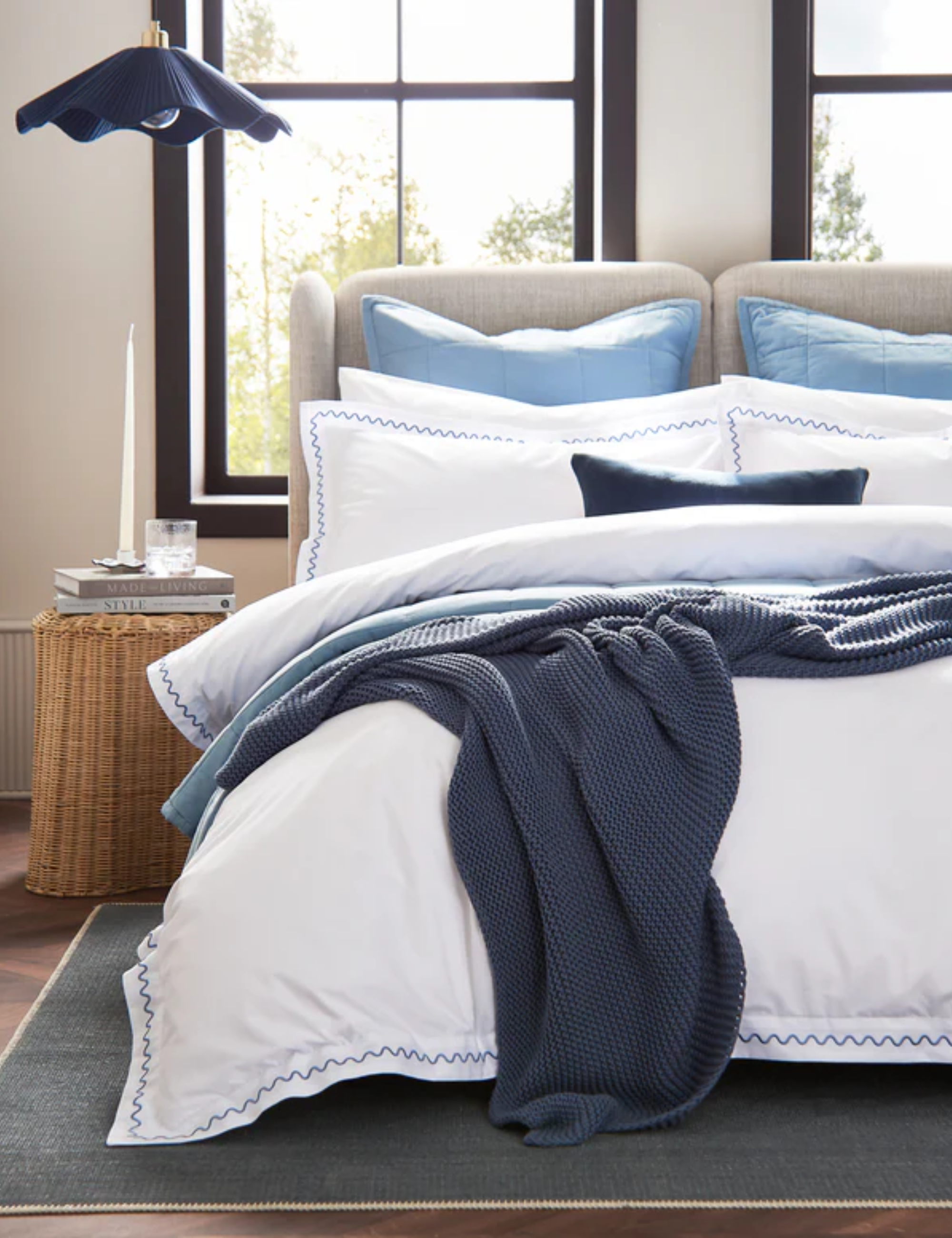 Christy bedscape featuring squiggle-border cotton sheets, blue pillowcases, and a navy woven throw