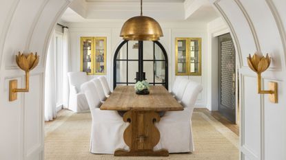 White dining room with wood dining table and antique brass light fixtures