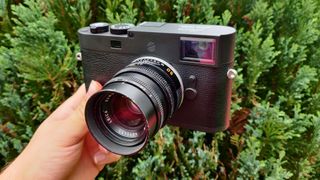 Leica M11-D held in the hand in front of a green bush