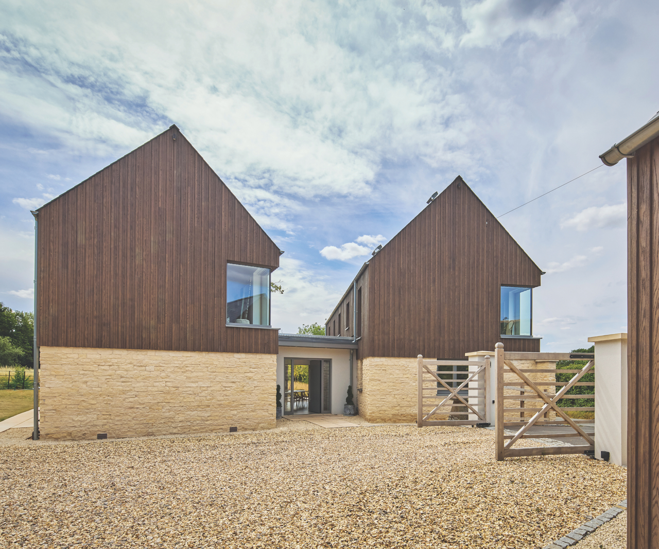 Side profile of wood cladded houses connected by a hallway in the middle and gravel in front