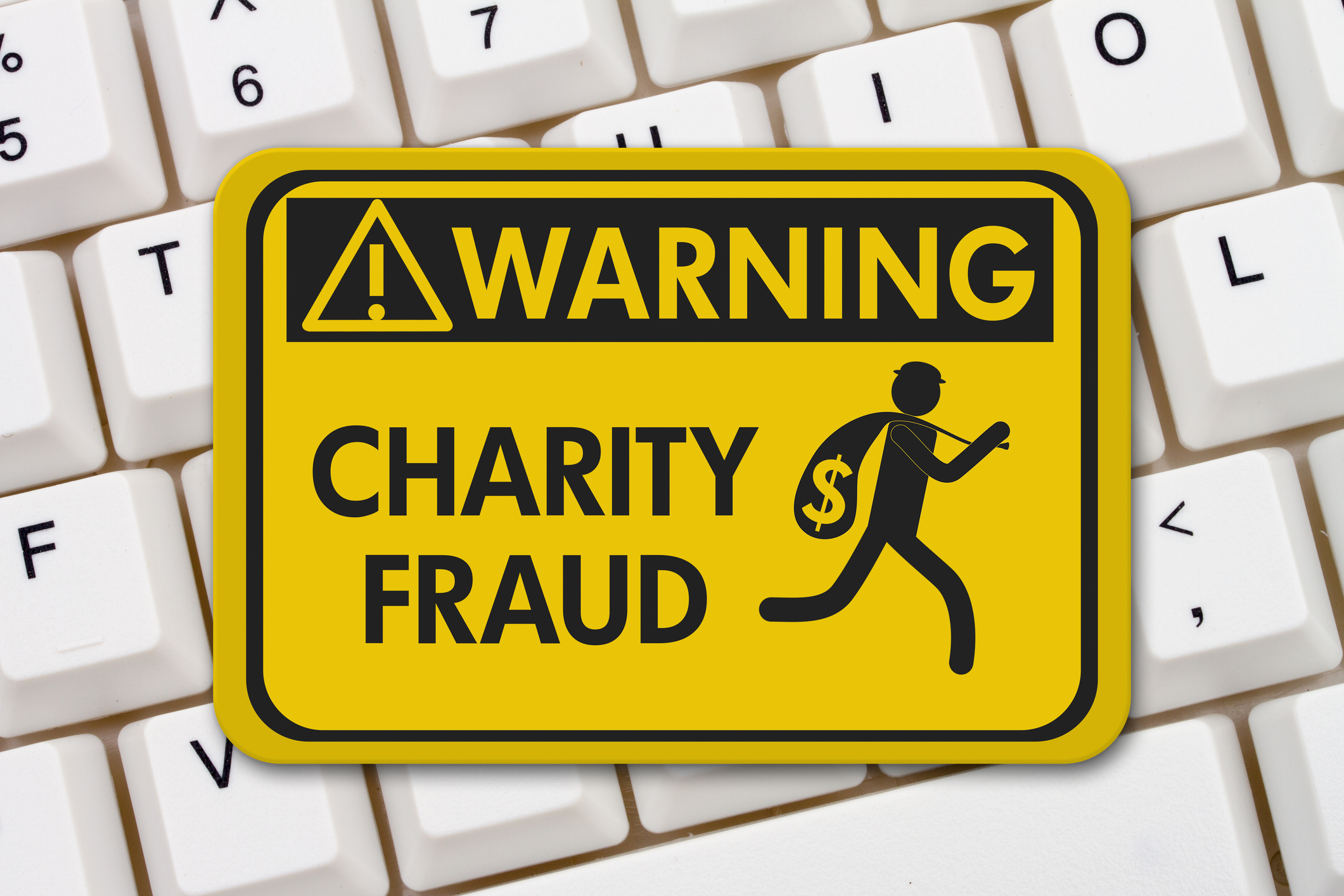 a keyboard with a yellow caution sign on top warning of charity scams