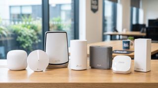 Mesh Wi-Fi routers on a table showing the Google Nest Wifi Pro, TP-Link Deco M5, Netgear Orbi WiFi 770, TP-Link Deco BE65, Asus ZenWiFi AX (XT8), Amazon Eero 6+, Linksys Velop WiFi 6 AX4200