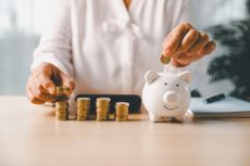 A person adding coins to a white piggy bank