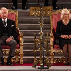 Queen Camilla and King Charles wearing black outfits sitting on thrones