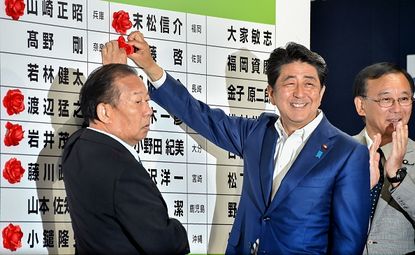 Japanese Prime Minister Shinzo Abe places a rosette next to the name of a parliamentary winner on Sunday.