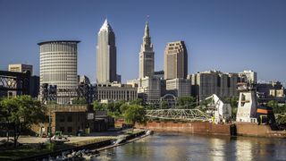 A photograph of Cleveland skyline showing a number of tall skyscrapers and a river in the foreground.