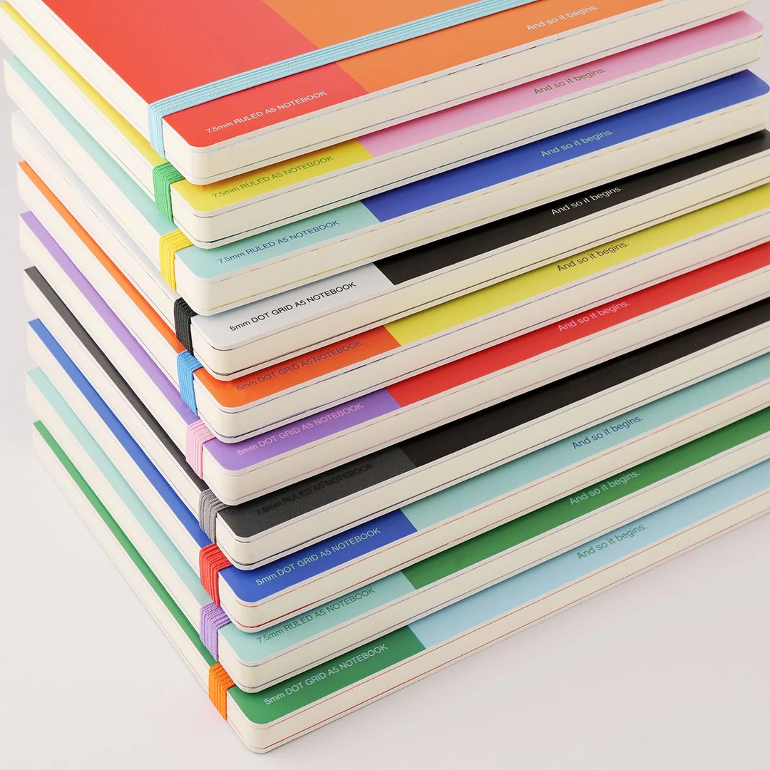A stack of color-blocked notebooks against a white wooden table.