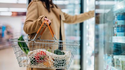 Person holding shopping basket in supermarket aisle