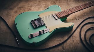 A Harley Benton TE-62LA on a distressed concrete floor with a guitar cable coiled nearby