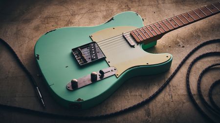 A Harley Benton TE-62LA on a distressed concrete floor with a guitar cable coiled nearby