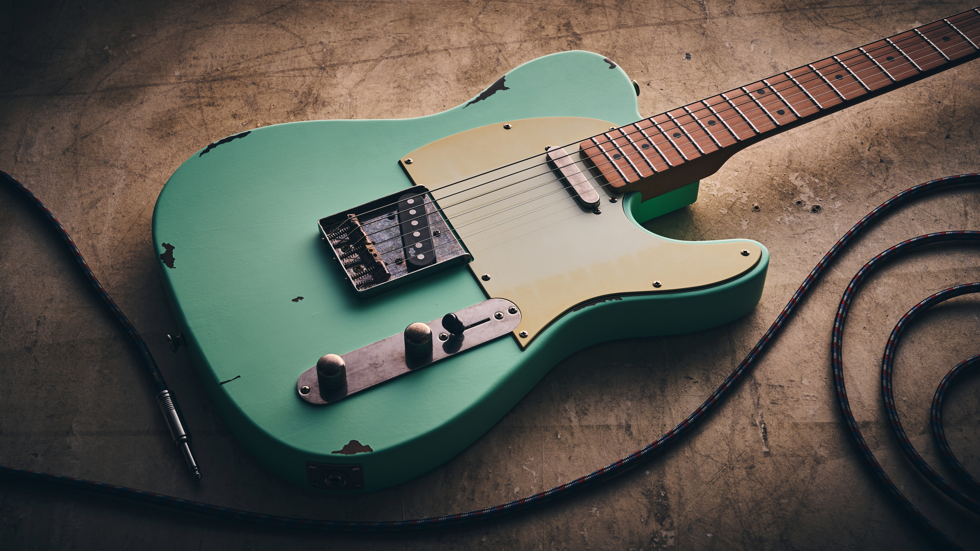 A Harley Benton TE-62LA on a distressed concrete floor with a guitar cable coiled nearby