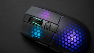 En svart Roccat Burst Pro Air ligger på en svart yta och lyser i lila och blå RGB-färger.