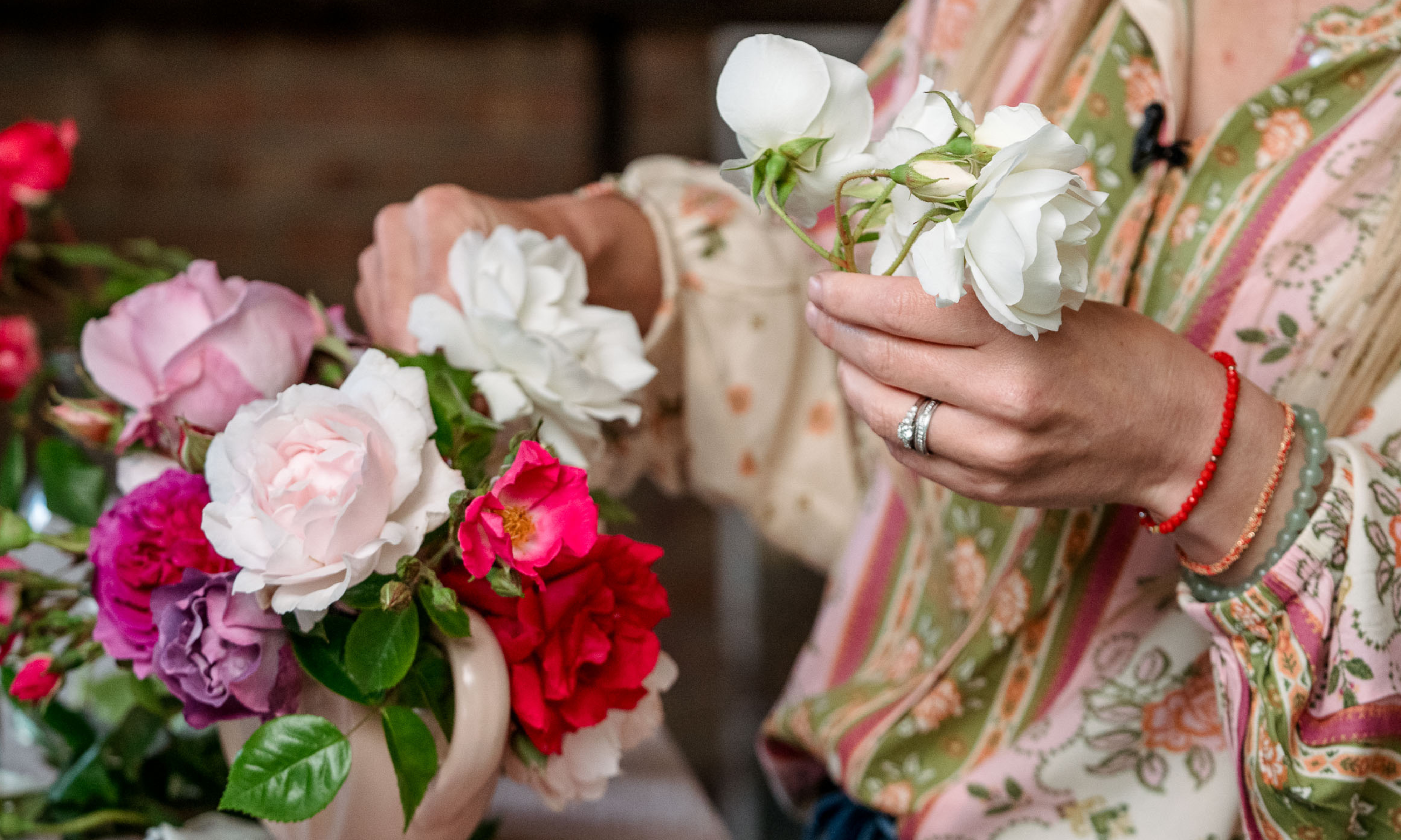 Hands making a garden rose floral design in pink vintage vase