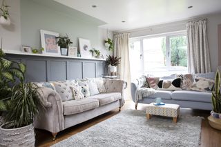 Living room with grey panelling to dado height, pastel green paint extending above and onto ceiling over shelving, pink sofa and grey sofa, wood flooring and grey rug