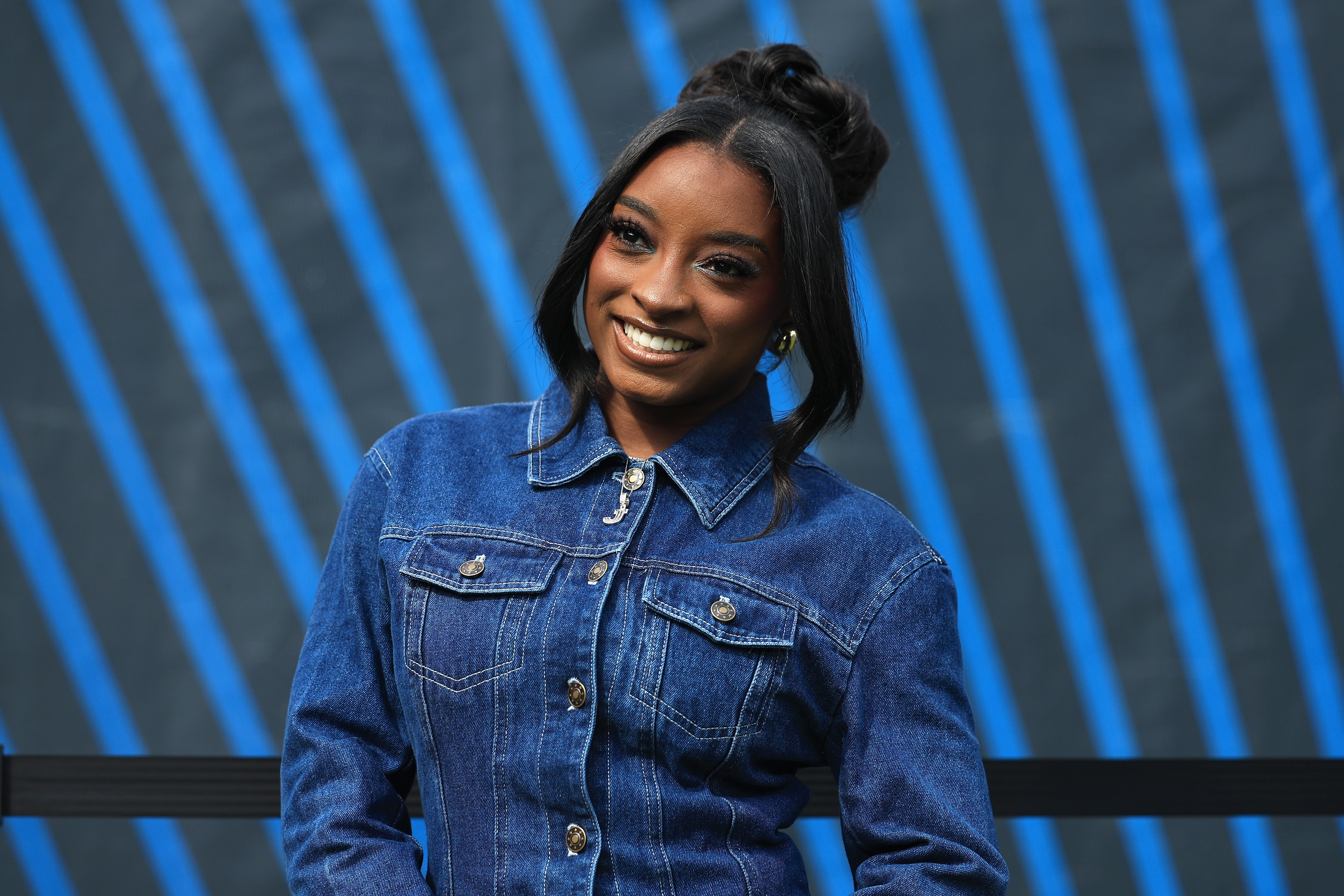 Simone Biles wearing a denim shirt buttoned all the way up with a Pamela Anderson updo hairstyle