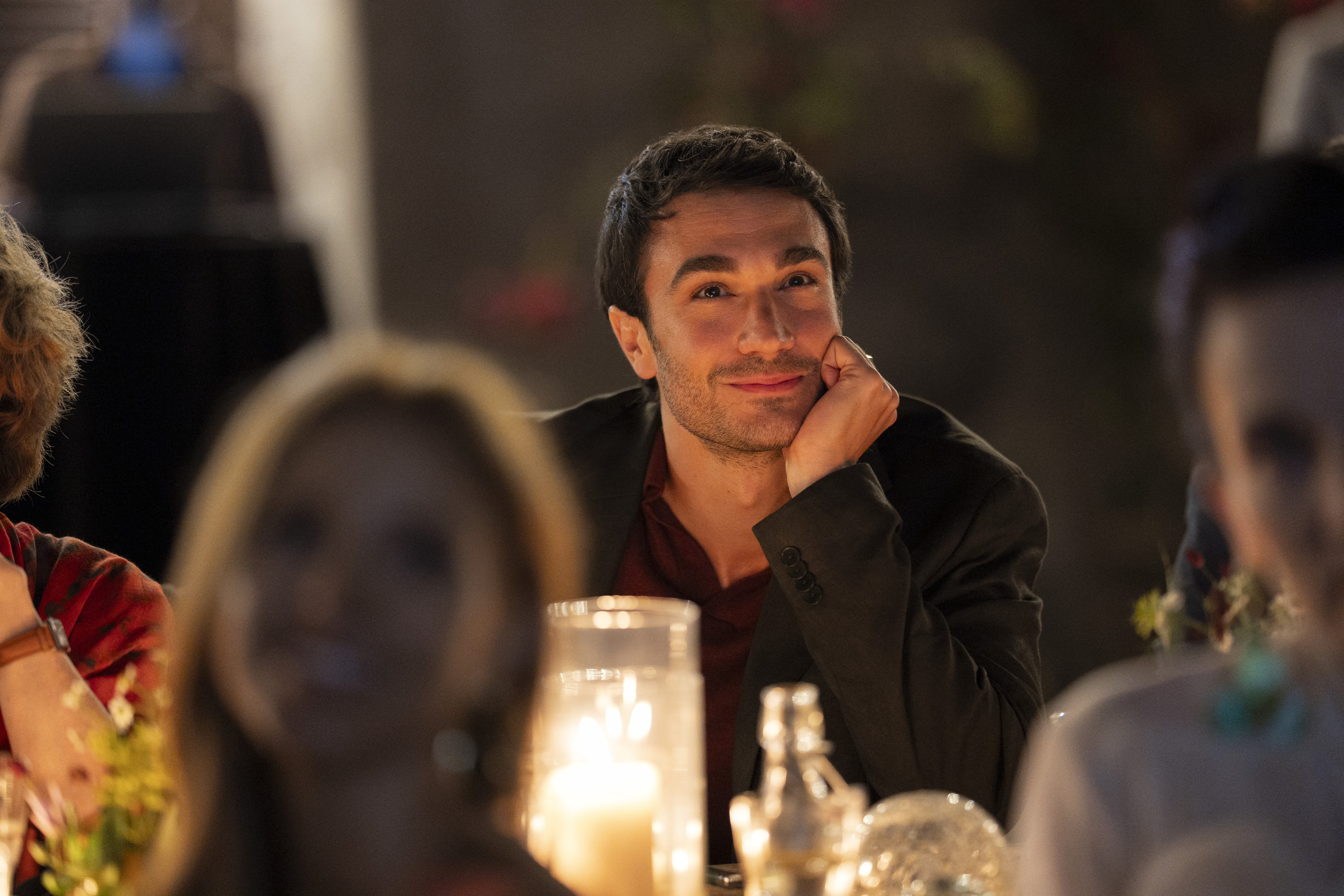 A man (Eugenio Franceschini as Marcello) gives an admiring look while leaning his head on his hand, at a candelit table during a party, in episode 504 of 'Emily in Paris.'