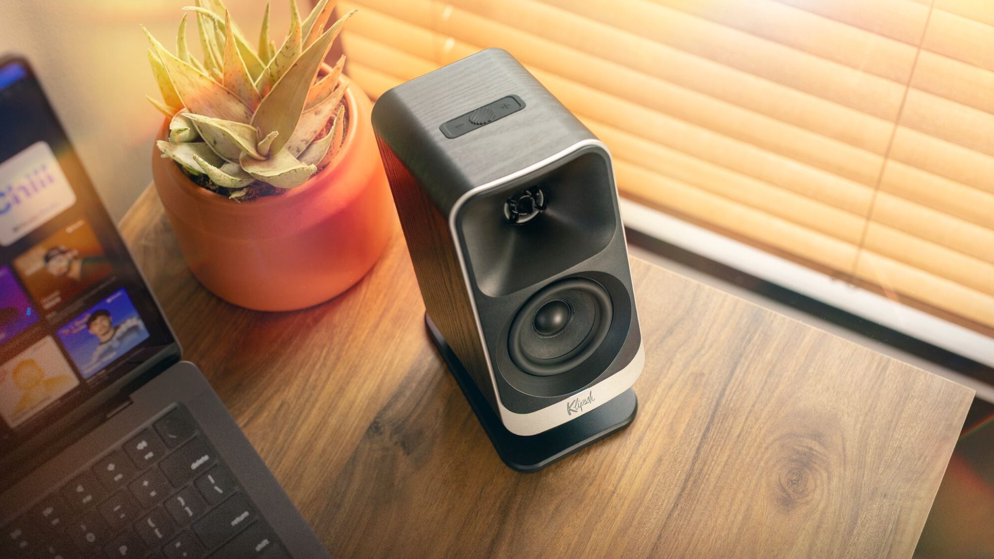 Lifestyle image of the Klipsch ProMedia Lumina speaker shot from above, next to a laptop on a wooden desk