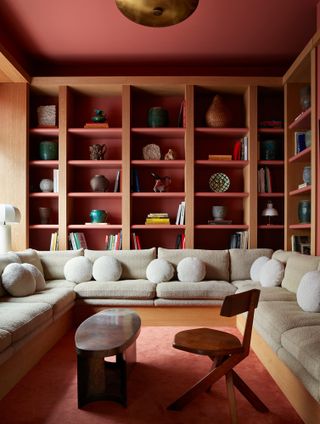Living room featuring oak bookshelves with recesses painted red, red ceiling, red carpet and beige built-in U-shaped seating