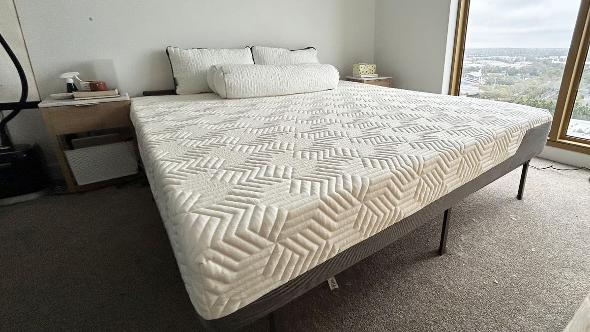 Valmori Hybrid II mattress on bed frame with four pillows in bedroom with two nightstands and window to the right