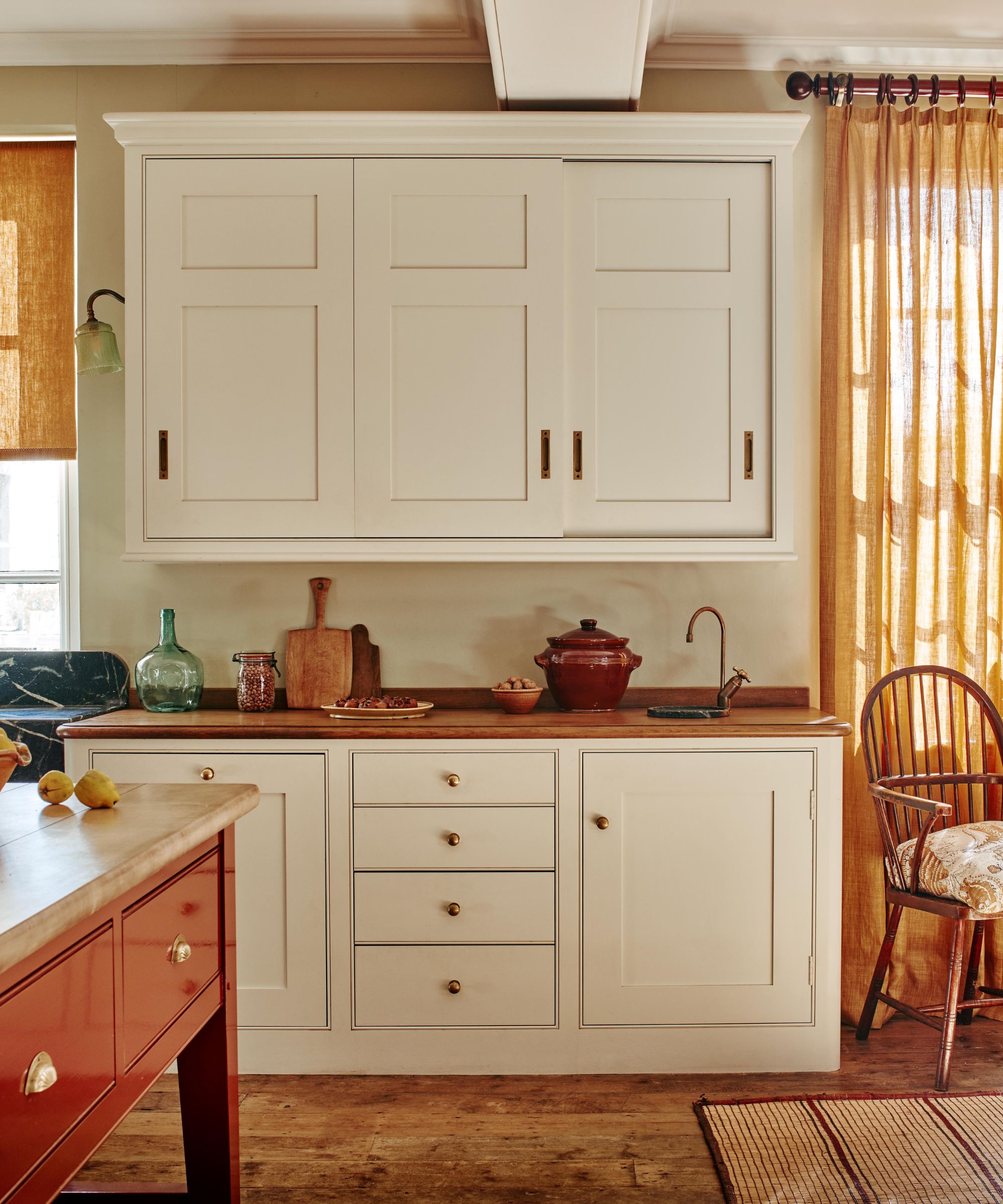 A traditional kitchen with white cabinets, wood countertops, and a terracotta red island