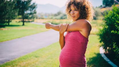 Pregnant woman stretches while exercising outdoors