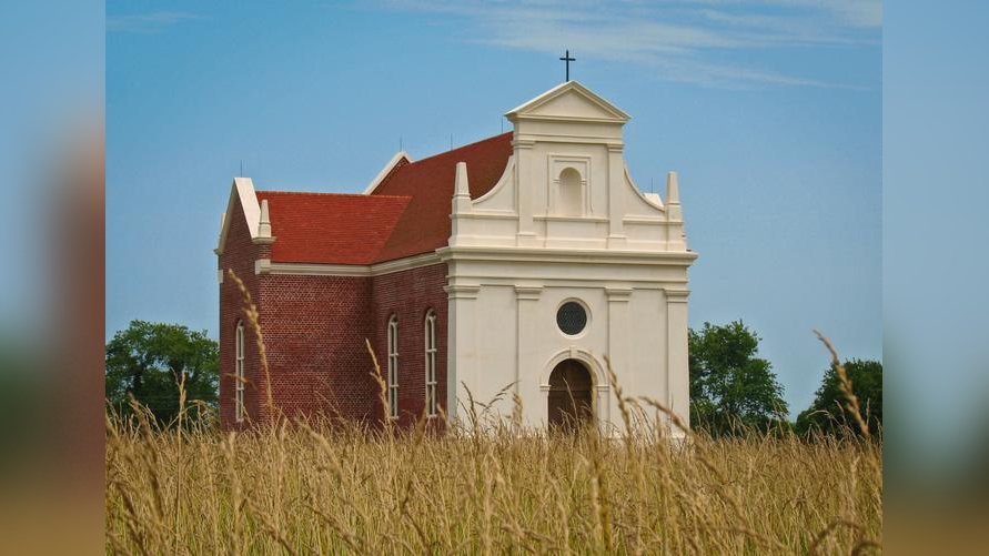 a small white and brick church in a field of dried grass