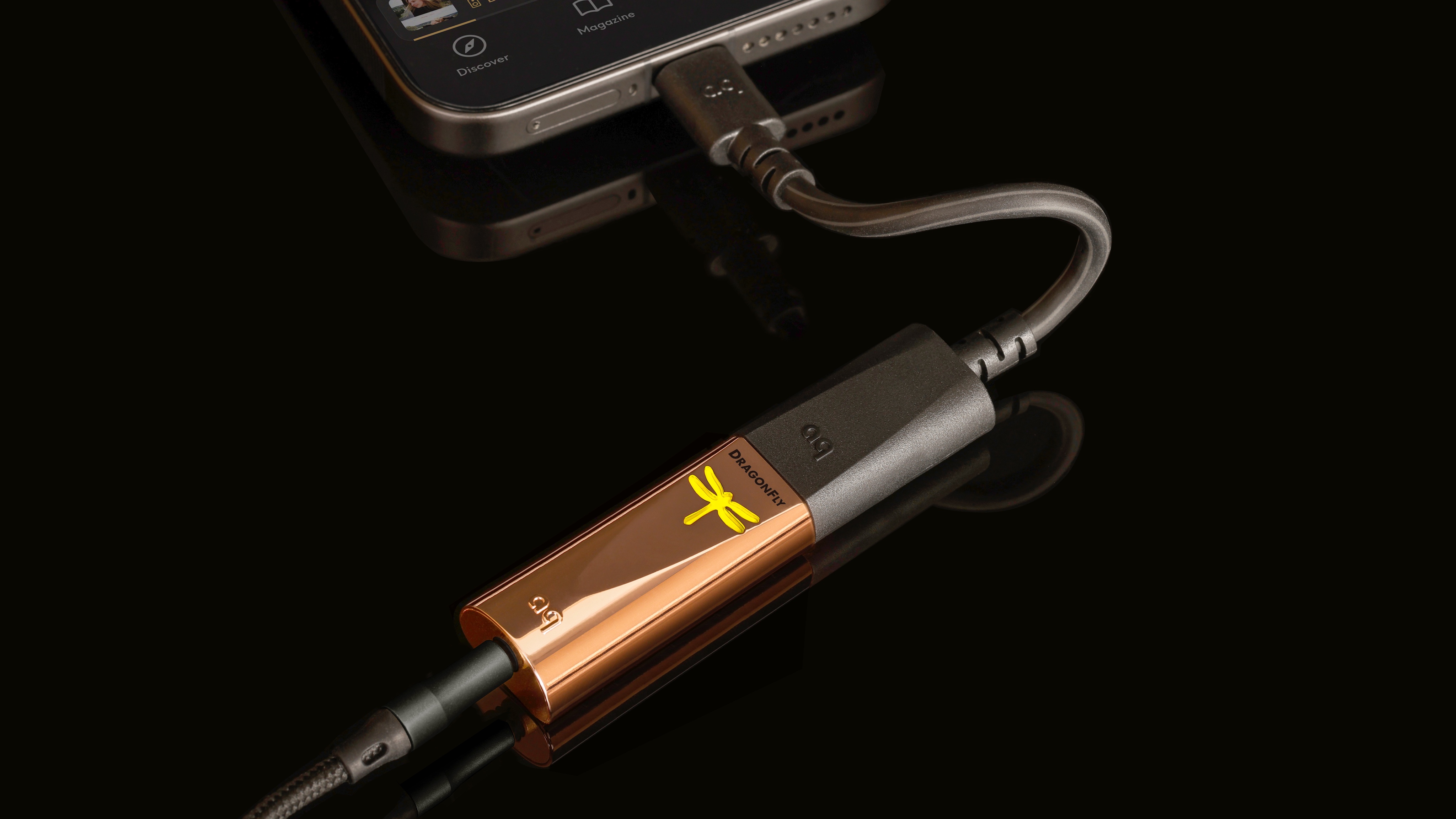 The AudioQuest DragonFly Copper plugged into a phone on a reflective black surface.