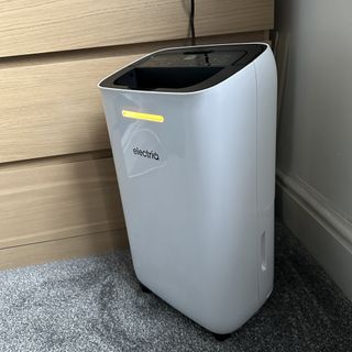 The ElectriQ 12L dehumidifier with its humidity indicator light lit up green in a room with a grey carpet