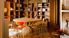 Round office with floor-to-ceiling wood joinery and shelving, wooden floor, large round sculptural wooden table and metal and plastic chairs