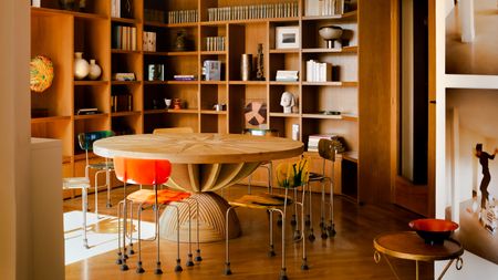 Round office with floor-to-ceiling wood joinery and shelving, wooden floor, large round sculptural wooden table and metal and plastic chairs