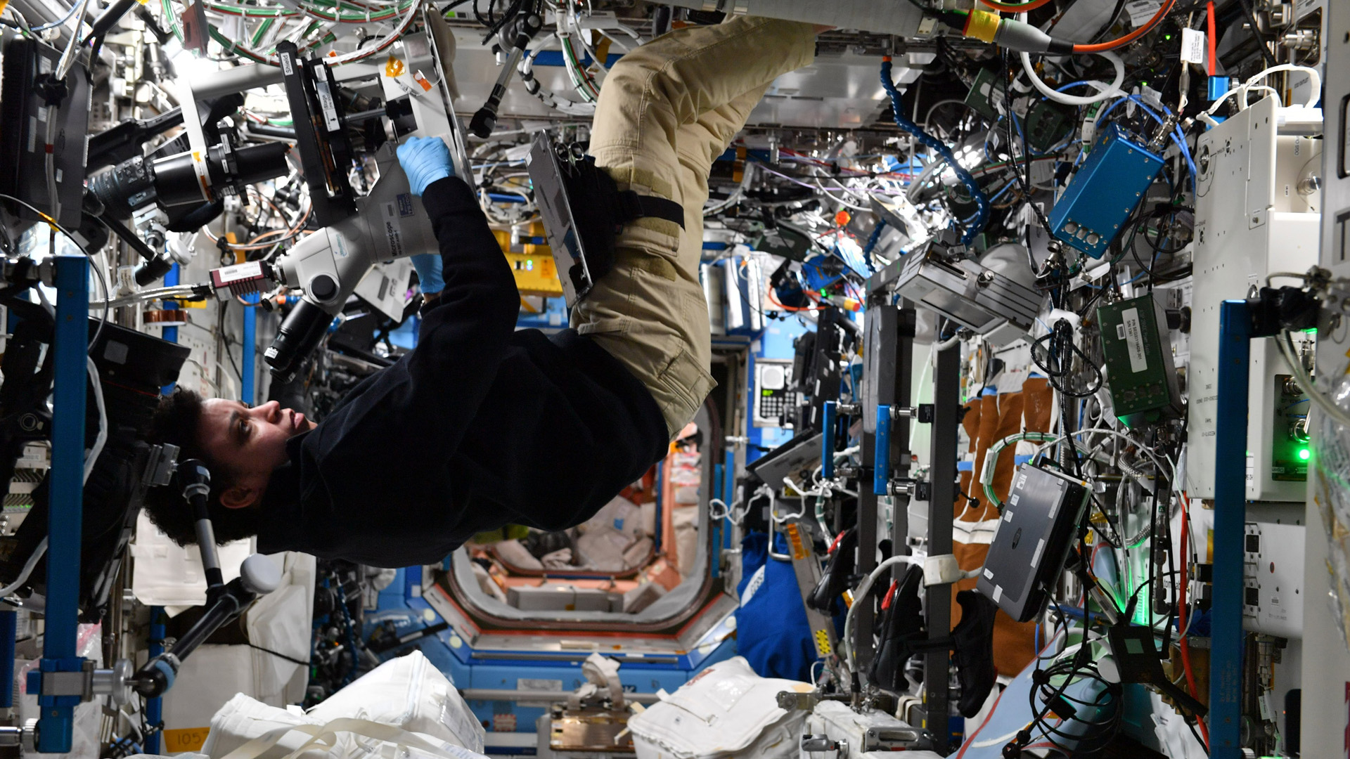 astronaut floating in iss surrounded by experiments