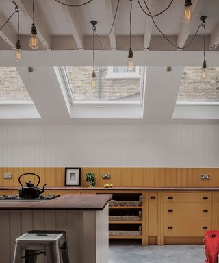 Exposed bulbs in an industrial style kitchen island lighting idea, with mustard painted cabinets and tongue and groove panelling on the walls.