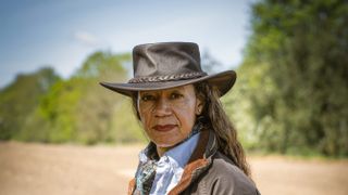 Farmer Celia wearing a cowboy style hat with a field backdrop.