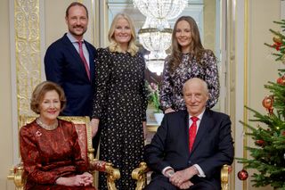 King Harald, Queen Sonia, Crown Prince Haakon, Crown Princess Mette-Marit and Princess Ingrid Alexandra posing next to a Christmas tree in suits and dresses