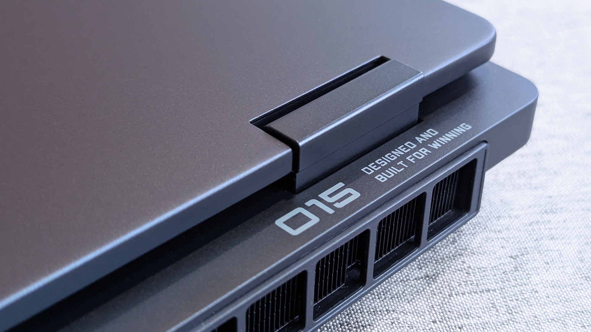 A close-up of the HyperX OMEN 15 laptop&amp;rsquo;s rear hinge and cooling vents, with printed text near the hinge reading &amp;ldquo;O15 DESIGNED AND BUILT FOR WINNING.&amp;rdquo;
