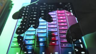 A translucent hand in shadow typing on a colourful keyboard