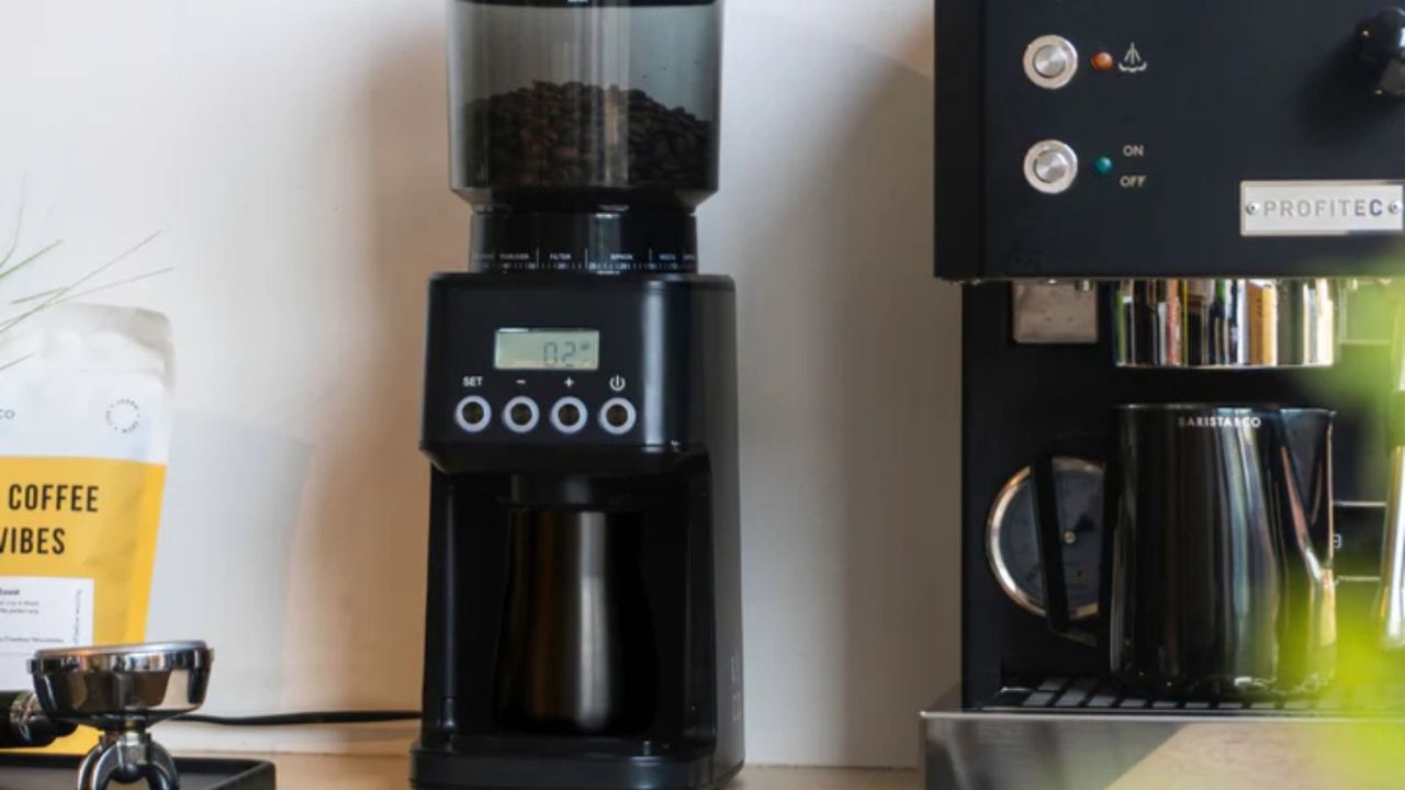 Barista &amp; Co Core All Grind Plus Grinder on a countertop next to a coffee maker with a coffee bag to the left