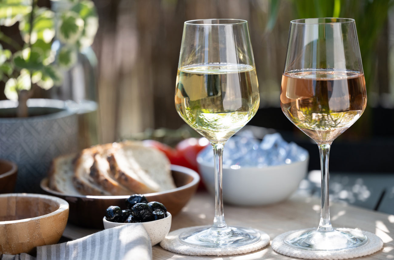 A glass of white wine and glass of ros&eacute; with food in outdoor setting