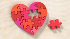 A heart made of puzzle pieces with one piece in the middle sitting off to the side.