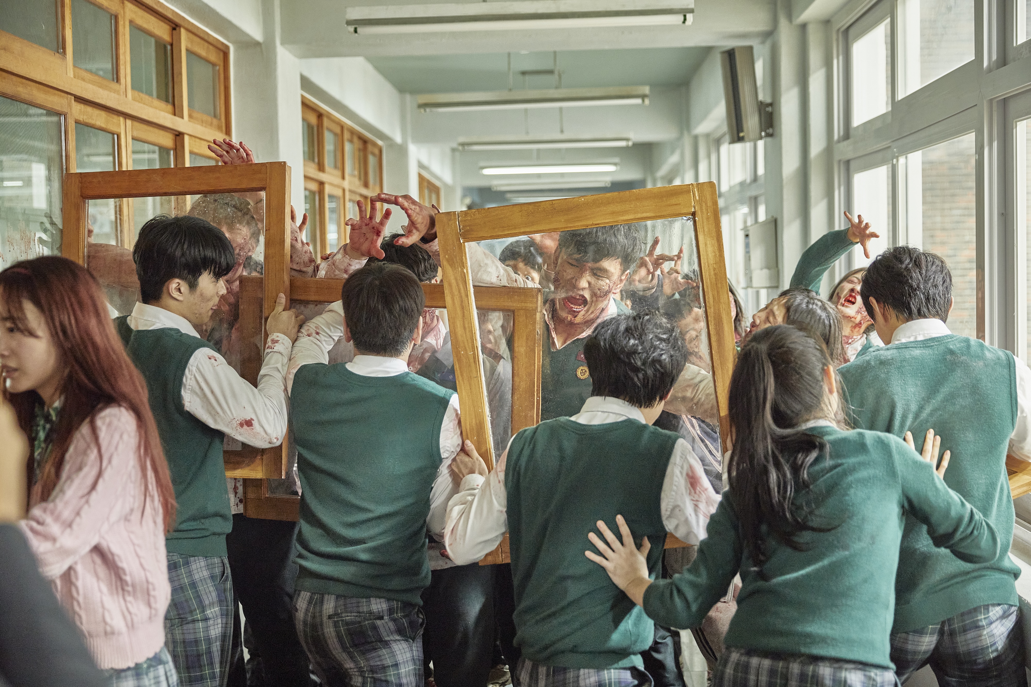 A group of Korean high-school students use wood-framed glass panels to defend themselves against a horde of zombies, also wearing school uniforms and splattered in blood. A still from the Netflix K-drama 'All of Us Are Dead.'
