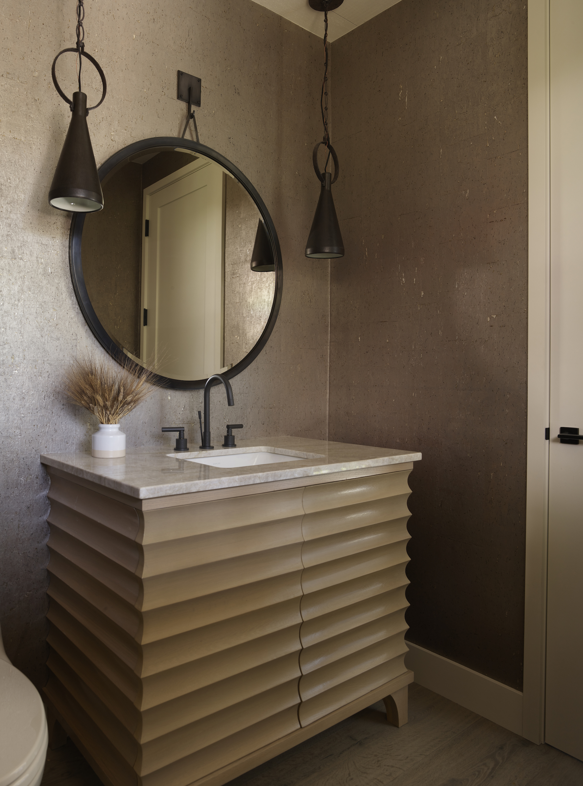 neutral powder room with ribbed vanity unit, marble countertop, round mirror and pendant lights